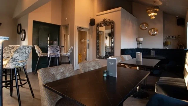 A table set with a menu in front of a blue banquette and ornate mirror